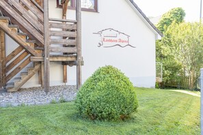 Een gebouw met een houten trap, een bord met de tekst 'Landhaus Alpena' en een verzorgd gazon.