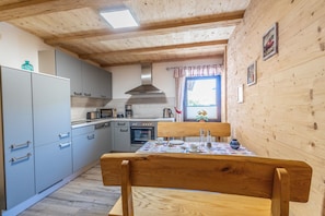 Een keuken met houten balken in het plafond, grijze kastjes, een magnetron en een eettafel.