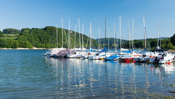 A marina with multiple sailboats docked, calm water, and a forested hillside in the background. - Apartment 'Fewo Wendelstein' with Shared Terrace, Shared Garden and Wi-Fi (Willingen (Upland))