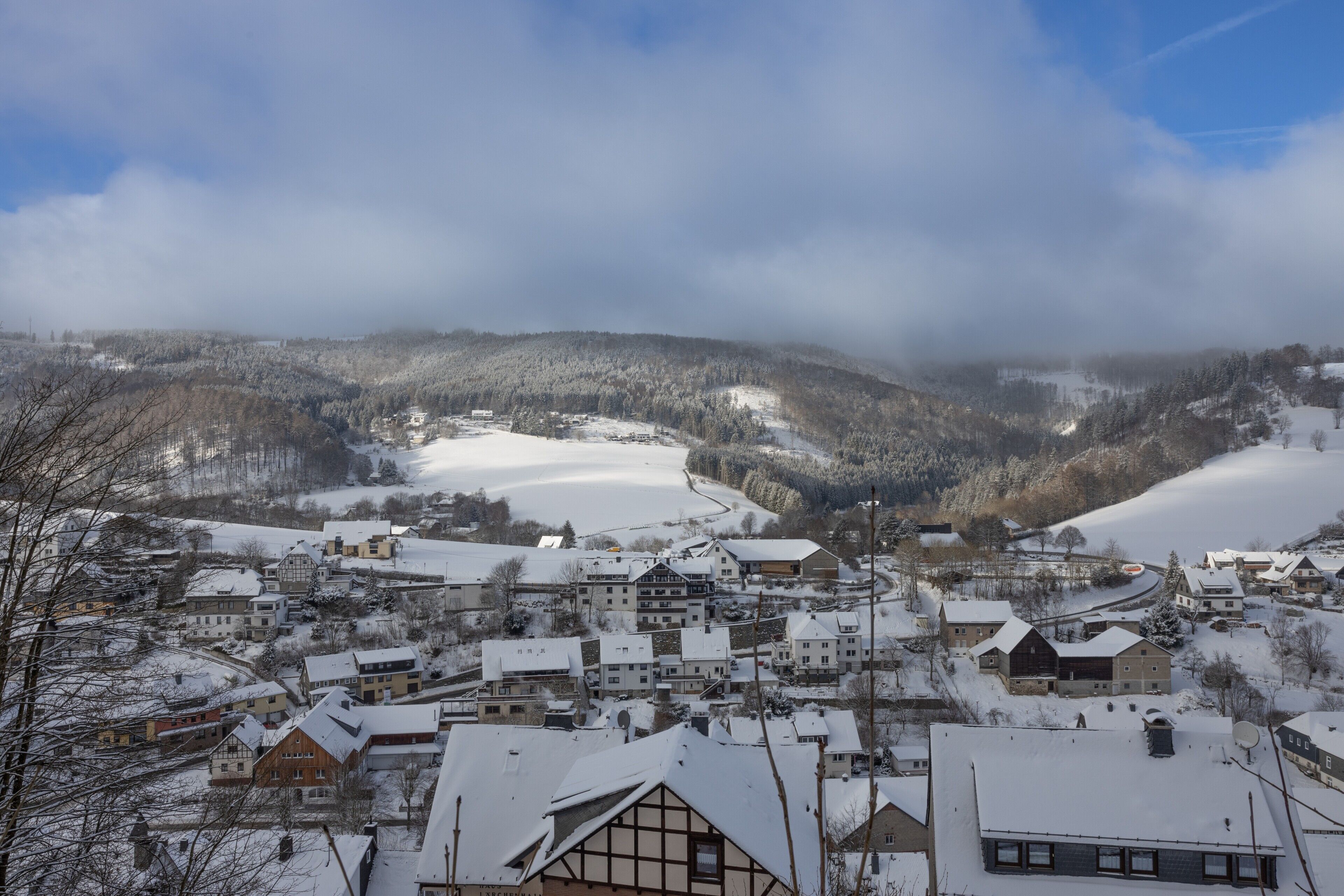 A snow-covered village with traditional buildings, a winding road, and a valley.