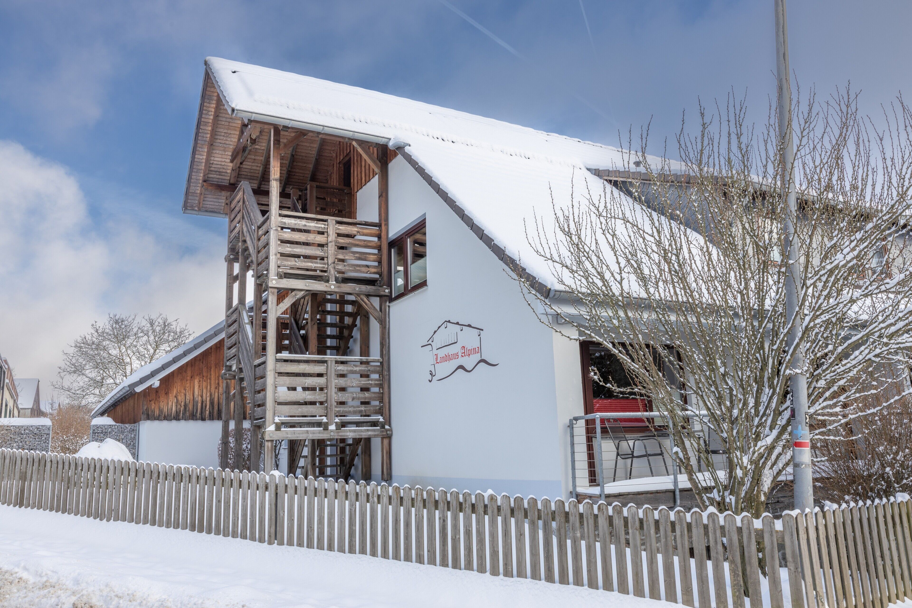 A building with a wooden staircase, a balcony, and a snow-covered roof.
