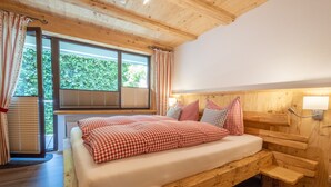 A wooden bed with a checkered blanket, a window with blinds, and a lamp on the wall. - Apartment 'Fewo Wendelstein' with Shared Terrace, Shared Garden and Wi-Fi (Willingen (Upland))