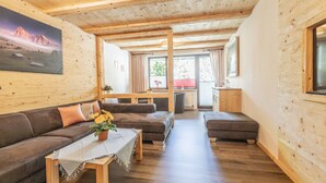 A wooden interior with a sofa, ottoman, and table, a painting on the wall, and a window with curtains. - Apartment 'Fewo Wendelstein' with Shared Terrace, Shared Garden and Wi-Fi (Willingen (Upland))