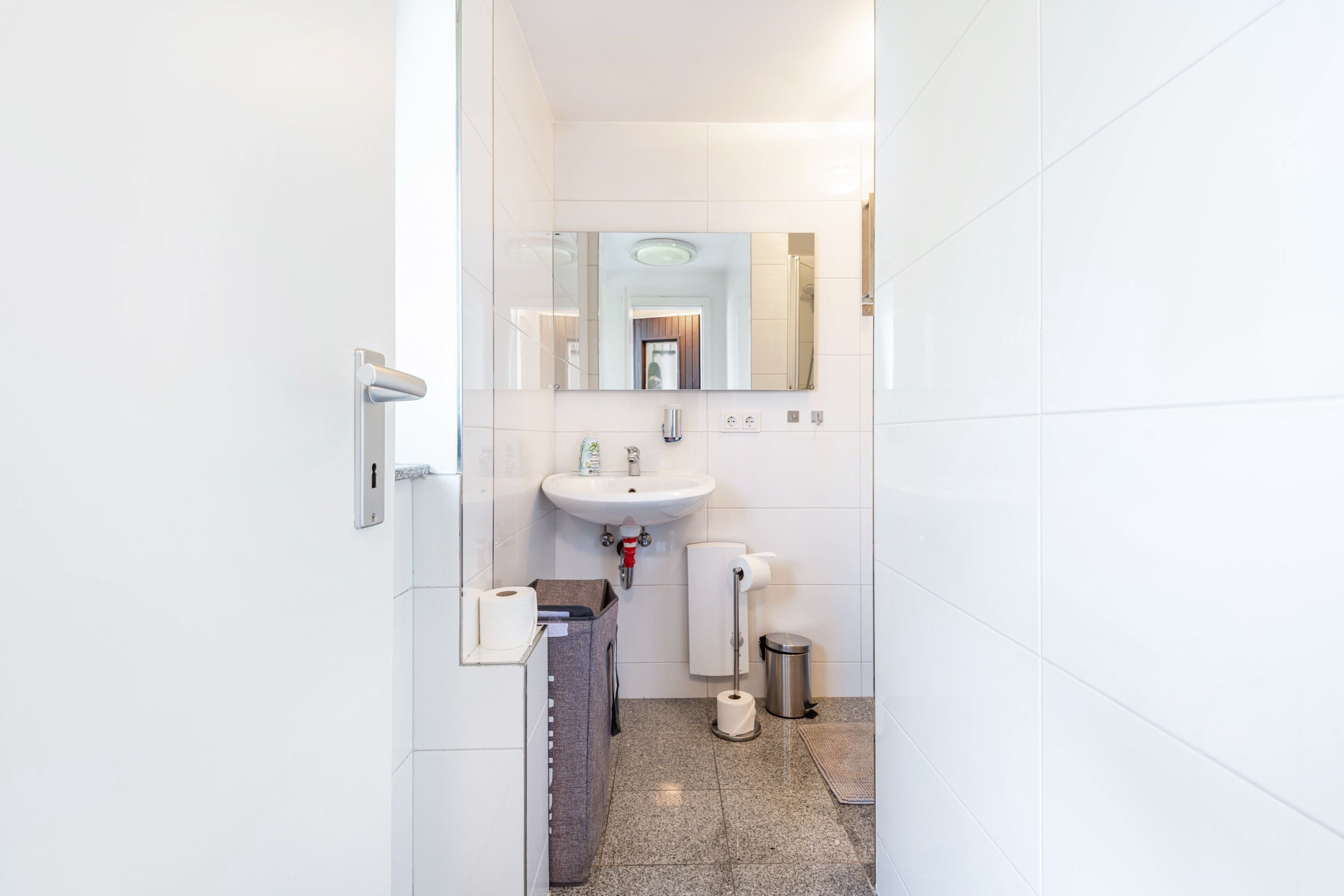 Un baño moderno con lavamanos, espejo, inodoro y cubo de basura.