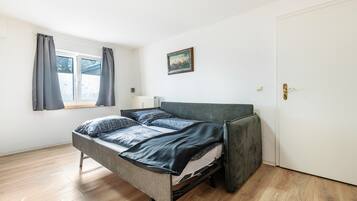 Een eenpersoonsbed met een grijs hoofdeinde in een kamer met houten vloeren en een witte deur.