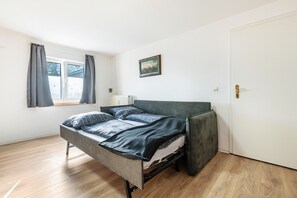 A single bed with a grey headboard in a room with wooden flooring and a white door.