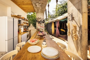Un espace de restauration extérieur rustique, avec une table en bois dressée pour deux personnes, un réfrigérateur et un coin cuisine équipé de divers ustensiles et ustensiles de cuisine.