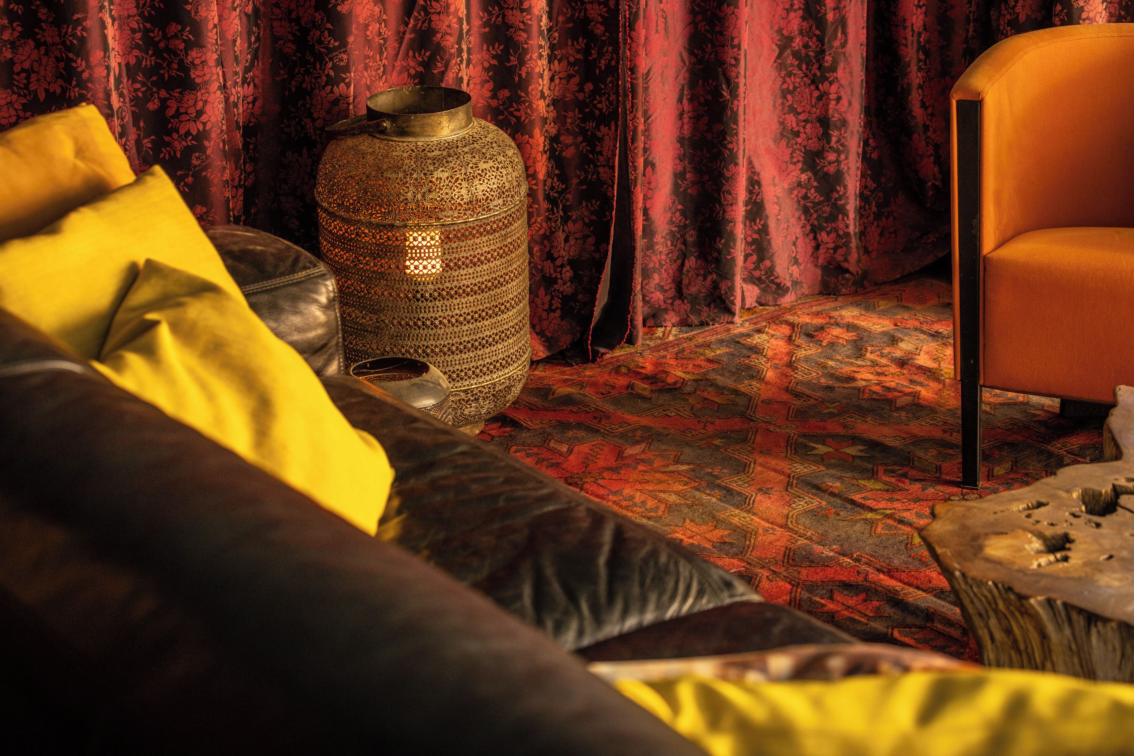 Una habitación con alfombra estampada, un sofá con cojines amarillos, un jarrón decorativo grande y una silla.