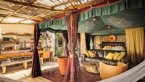 A cozy living area with a hammock, a sofa, and a coffee table. There is a large potted plant and a wooden bench. - Sultan's Tent at Caesarea by Sea N' Rent (Hof HaCarmel)