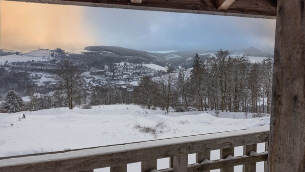 Un paisaje nevado con una terraza de madera y vistas a colinas cubiertas de nieve.