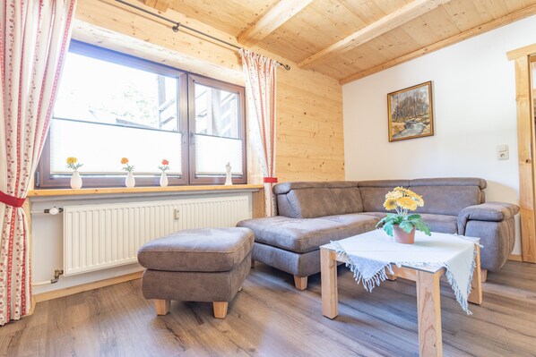 A cozy living room with a brown sofa, a small wooden table, and a window with curtains. - Apartment 'Fewo Rotwand' with Shared Terrace, Shared Garden and Wi-Fi (Willingen (Upland))