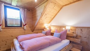 Un dormitorio de cabaña de madera con una cama, almohadas, una ventana y una mesita de noche.