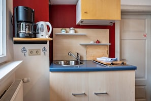 Et kompakt køkken med kaffemaskine, elkedel og reoler med krukker.