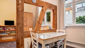 A room with a wooden-framed mirror, a white table with chairs, a bookshelf, and a window with a view of a building and greenery. - Studio Apartment 'Ferienwohnung Stralsund' with Wi-Fi (Stralsund)