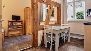 A room with a wooden beam structure, a television, a bookshelf, a table with a chair, and a window with a view of buildings and trees. - Studio Apartment 'Ferienwohnung Stralsund' with Wi-Fi (Stralsund)