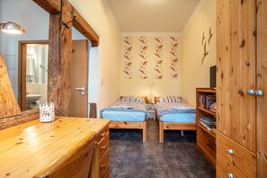 Quarto com duas camas de madeira, um guarda-roupa de madeira, uma escrivaninha de madeira e um espelho.