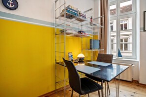 A room with a dining table, chairs, a lamp, a bookshelf, and a window with a view of buildings. - Studio Apartment 'Ferienwohnung Rügen' with Wi-Fi (Stralsund)