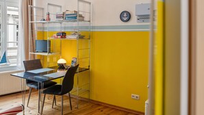 A room with a yellow wall, a metal shelving unit, a table with chairs, a lamp, and a window with curtains. - Studio Apartment 'Ferienwohnung Rügen' with Wi-Fi (Stralsund)