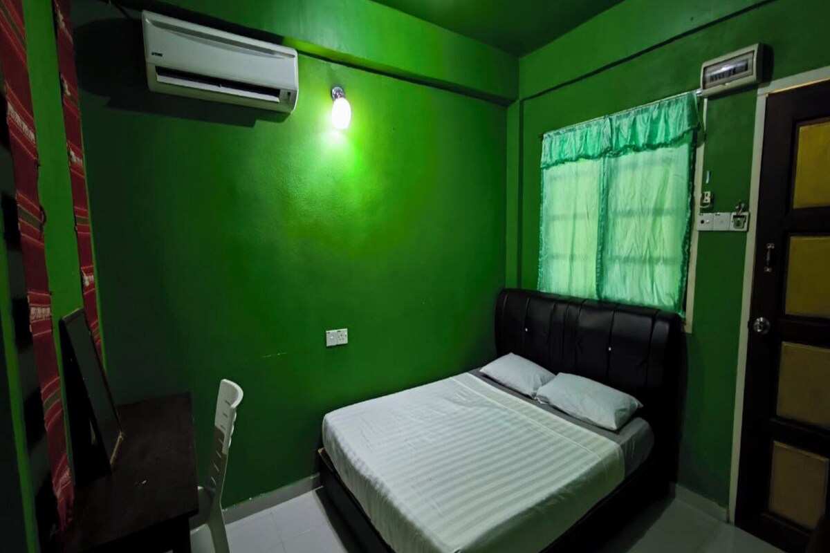 Een kamer met groene wanden, een bed met witte beddengoed, een zwart hoofdeinde en een airconditioning.