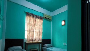 Een kamer met teal muren, twee eenpersoonsbedden, een kleine tafel, een raam met bloemen gordijnen en een airconditioning.