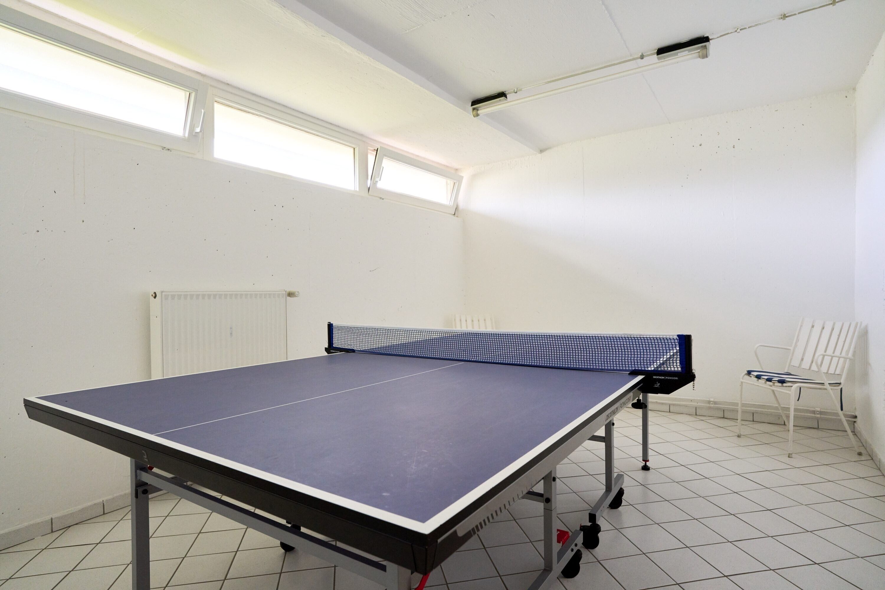 Una mesa de ping pong en una habitación con paredes blancas, un radiador y una ventana.