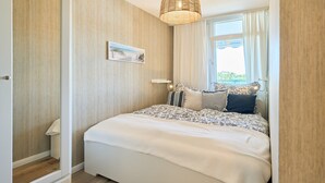 Une chambre à coucher avec un lit, un luminaire suspendu, une fenêtre avec des rideaux et un tableau accroché au mur.