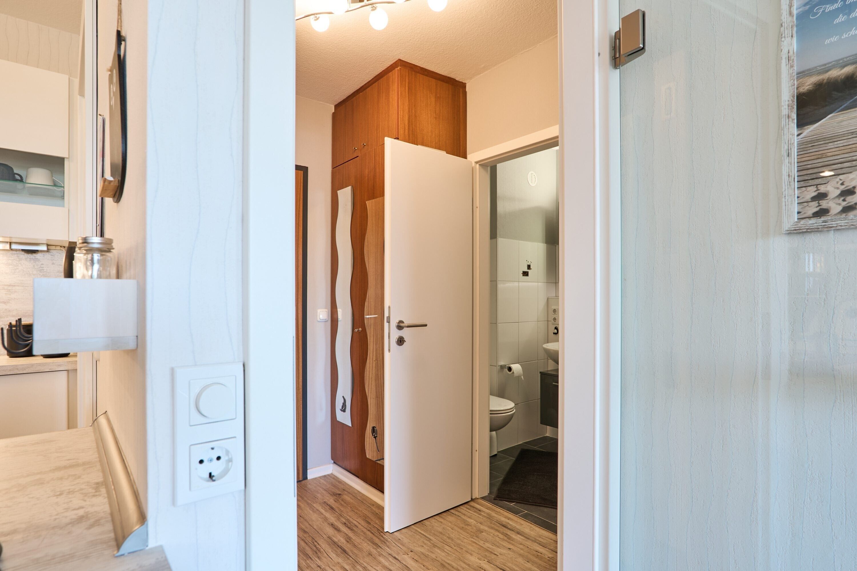 A hallway with a wooden door leading to a bathroom with a toilet and sink.