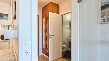 A hallway with a wooden door leading to a bathroom with a toilet and sink.