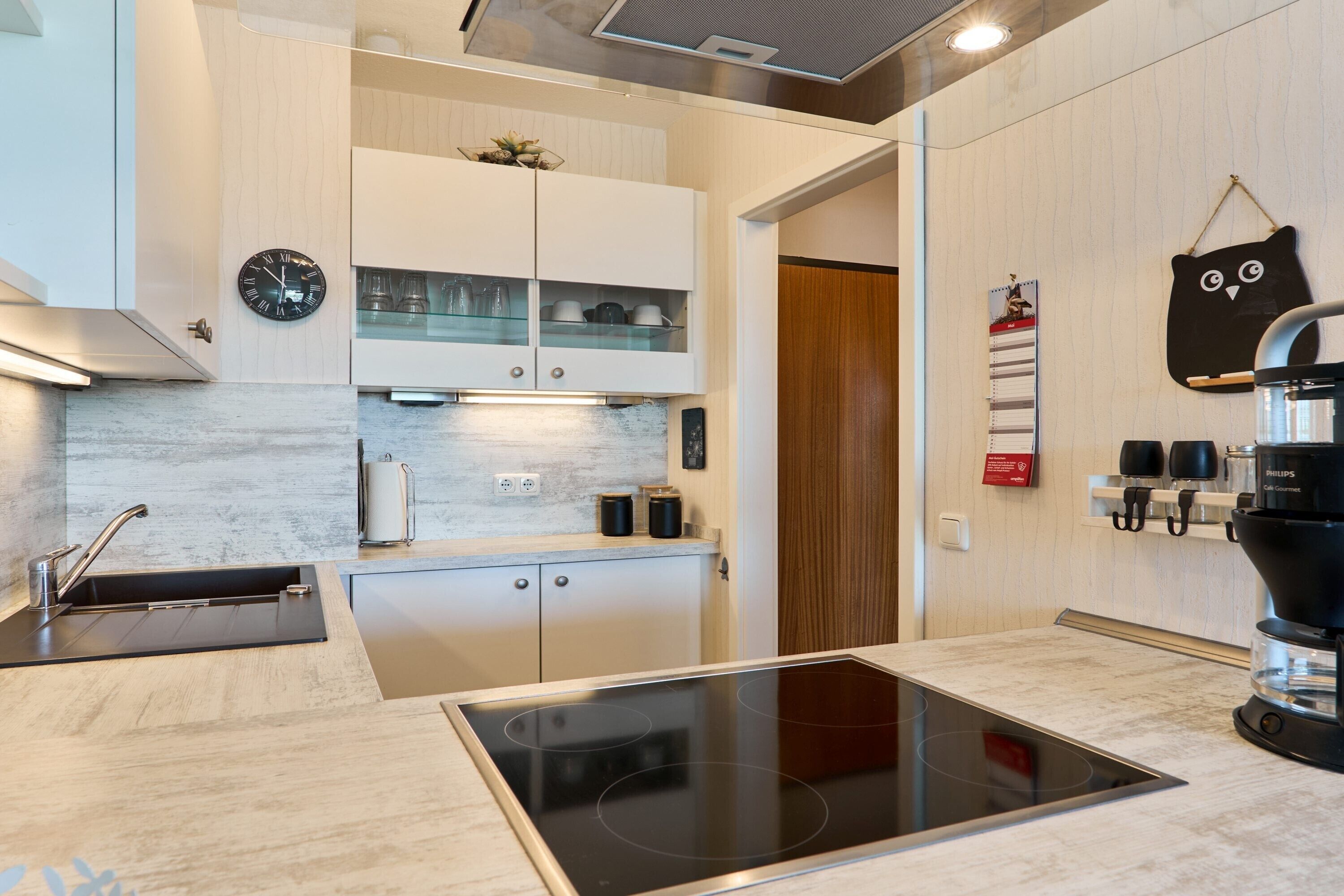 A modern kitchen with a built-in stove, white cabinets, and a coffee machine.