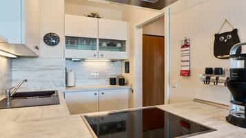A modern kitchen with a built-in stove, white cabinets, and a coffee machine.