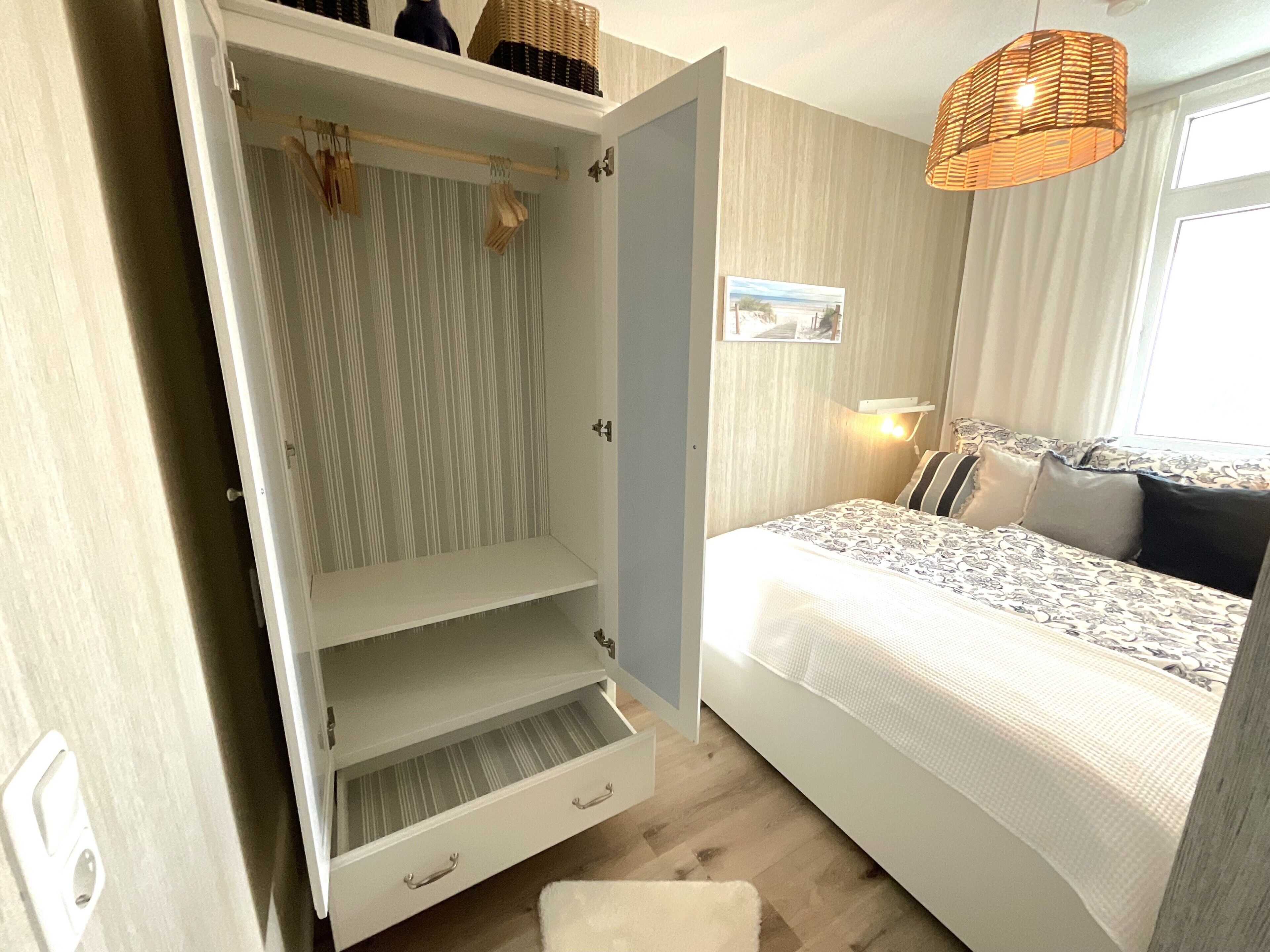 A bedroom with a bed, a wardrobe, a hanging light fixture, and a window.