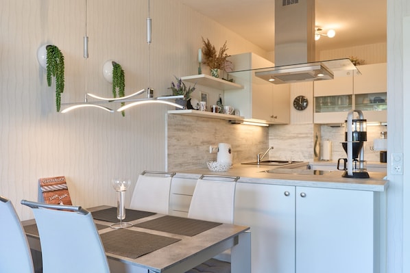Une cuisine moderne avec des meubles blancs, une table à manger avec des chaises et un luminaire suspendu.