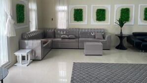 Un salon moderne avec un canapé d’angle gris, une petite table d’appoint blanche, un tapis gris et une table basse noire. Quatre couronnes vertes encadrées sont accrochées au mur.