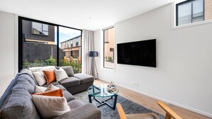 Ein modernes Wohnzimmer mit grauem Sofa, einem Glastisch und einem an der Wand montierten Fernseher.