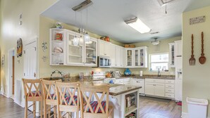 A kitchen with white cabinets, a wooden island with chairs, and a variety of kitchen appliances. - Steps to Crystal Beach! Family & Pet-Friendly Home (Crystal Beach)