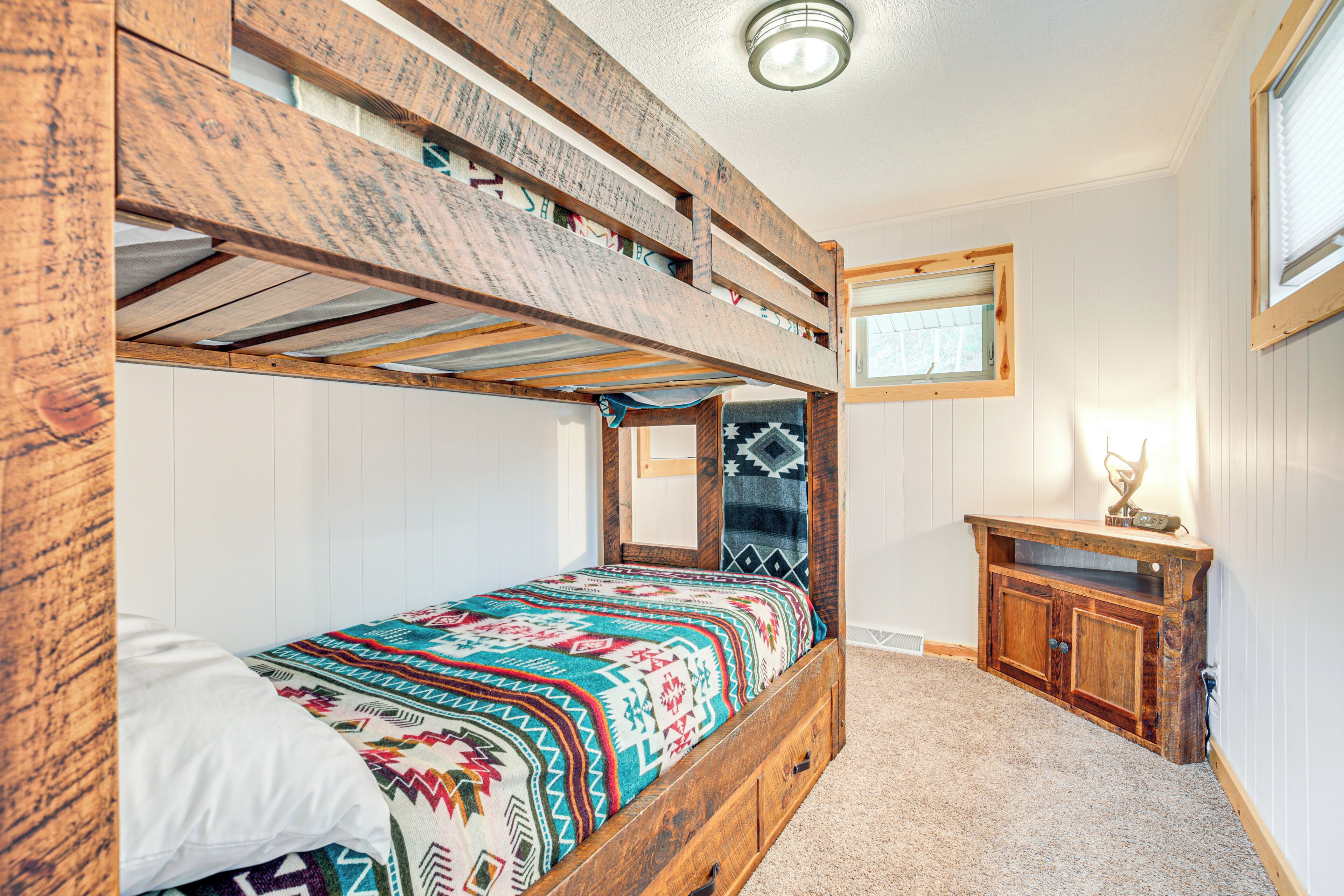 A bunk bed with a colorful blanket, a wooden dresser, and a window with blinds.