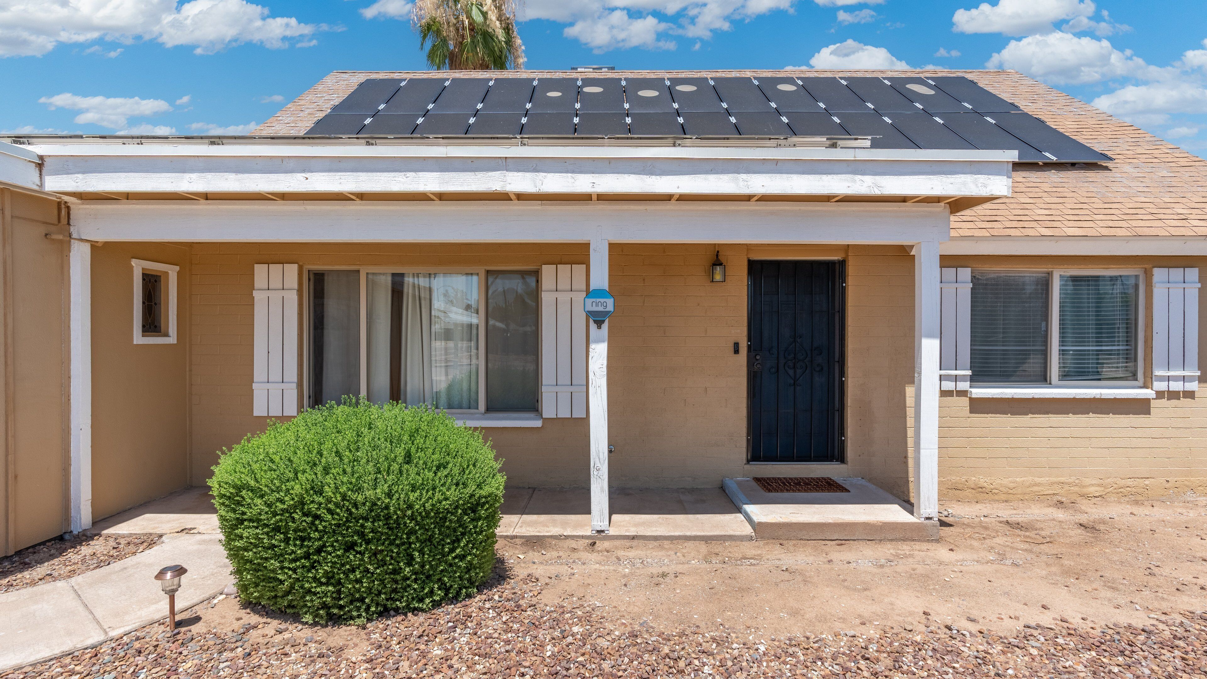 A single-story house with a covered porch, a small garden, and a solar panel roof.