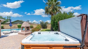 Ein Whirlpool in einem Garten mit Pool, Grill und einer Pergola.