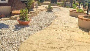 A residential property with a paved driveway leading to a house with a sloped roof and brick exterior. There are potted plants along the driveway and a view of a hilly landscape in the background. - Stunning Panoramic Waterfront Pool Home Escape (Anaheim)