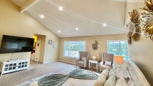 A spacious bedroom with a large bed, two armchairs, a TV, and a ceiling with recessed lighting. - Stunning Panoramic Waterfront Pool Home Escape (Anaheim)