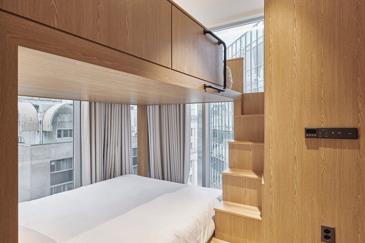 A modern bedroom with a large bed, wooden wardrobe, and a view of the city through large windows.