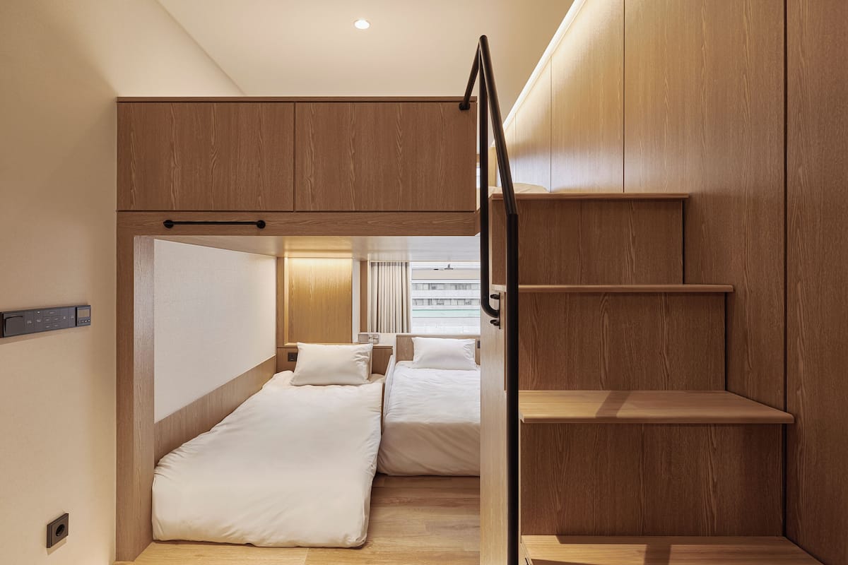 A compact, modern hotel room with two single beds, a small desk, and a built-in wardrobe.