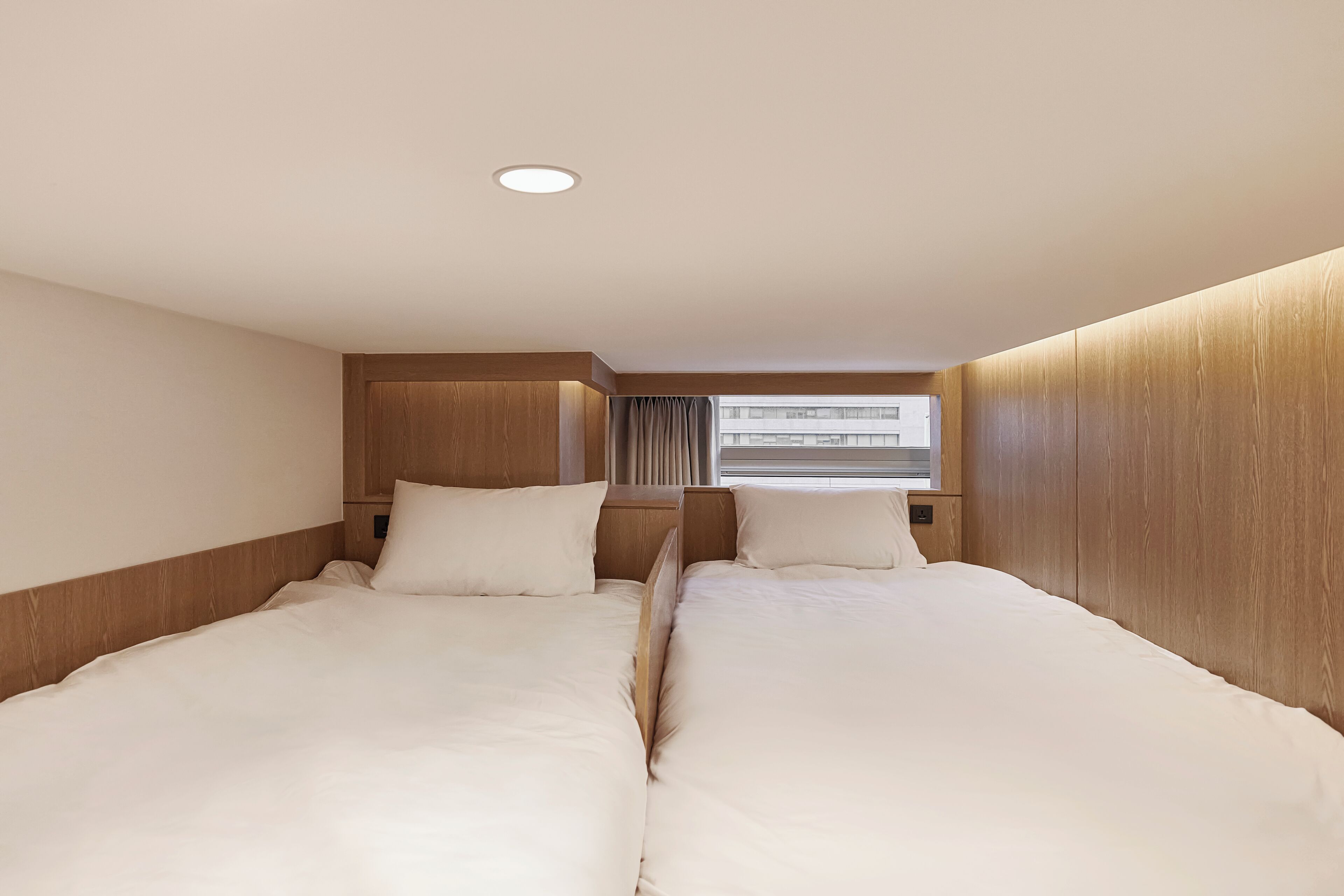 A hotel room with two beds, wooden paneling, a window with curtains, and a ceiling light.
