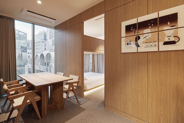 A modern hotel room with a wooden table and chairs, a large window with a city view, and a wall-mounted artwork depicting a coffee scene. - HOTEL DRIP&DROP Myeongdong (Seoul)
