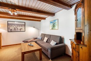 Un salon comprenant un canapé, une table en bois, un meuble, un tableau encadré et un plafond avec des poutres apparentes.