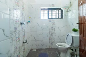 Ein Badezimmer mit weißen Marmorfliesen, einer Toilette, einer Duschkabine und einem kleinen Fenster.