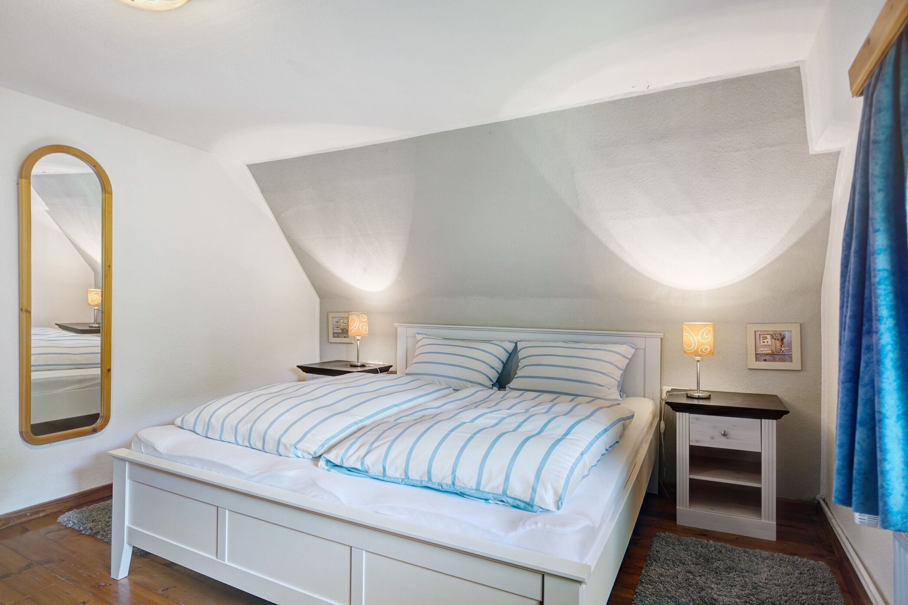 Ein Schlafzimmer mit Bett, Nachttischen, einem Spiegel und einer Deckenleuchte.