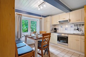 A compact kitchen with a dining area, wooden cabinets, a stove, and a window with curtains.
