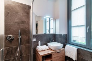 Un baño moderno con ducha, lavabo, espejo y ventana.