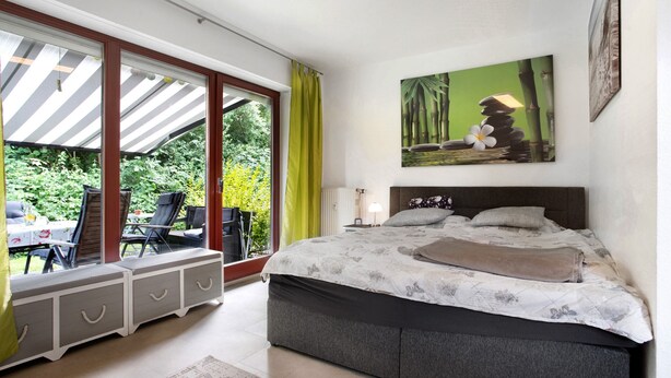 A bedroom with a bed, a window with curtains, a painting, and a view of greenery outside. - Apartment 'Ferienpark Gustow B09' with Shared Terrace and Shared Garden (Gustow)